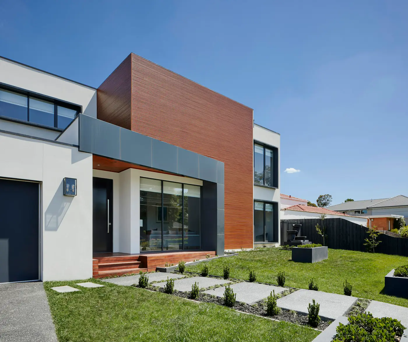 A modern house with a timber-clad facade and a lawn with stepping stones