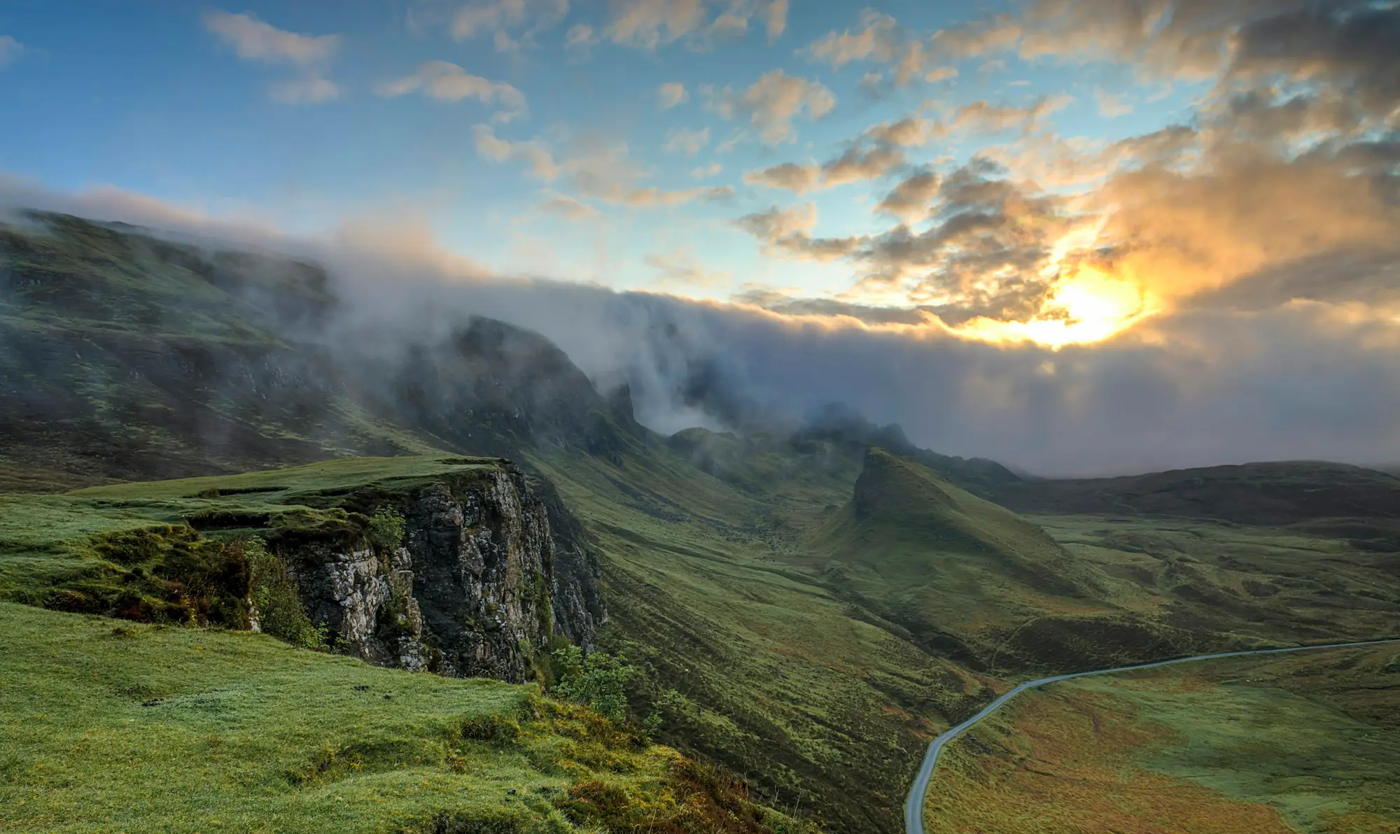 Misty green hills and valleys under a glowing sky